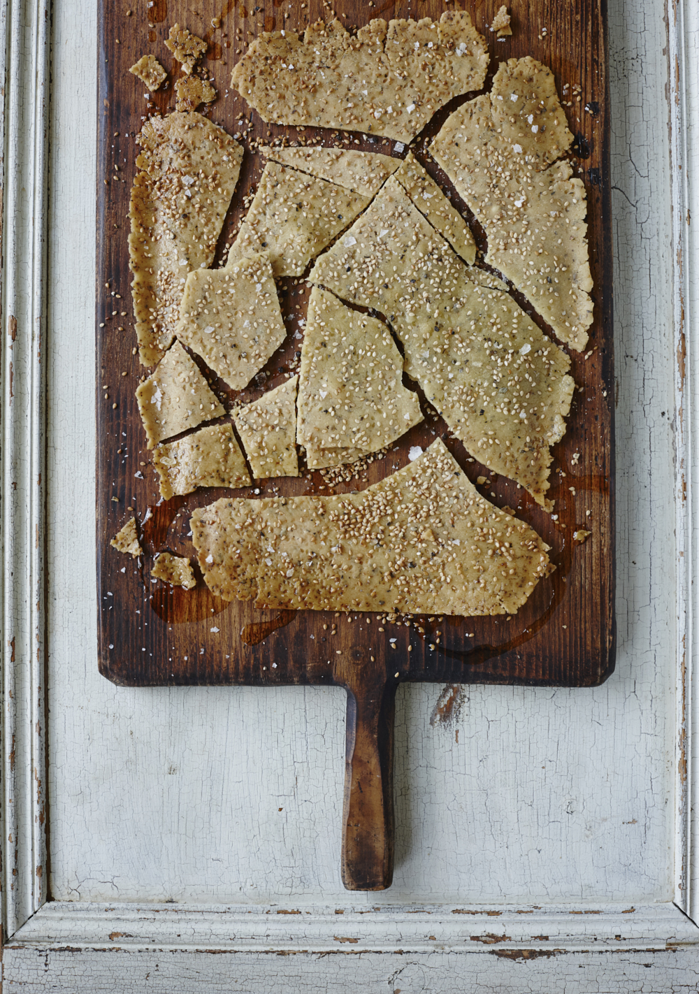 Rice snap flatbread made with sesame seeds, served on a wooden chopping board. Food photography by Joanna Henderson