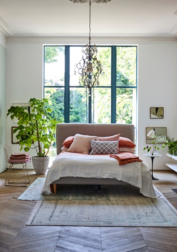 Bed with blush pink bed linen cushions and pillows on a parquet floor with green plantpot. Interiors photography by Joanna Henderson
