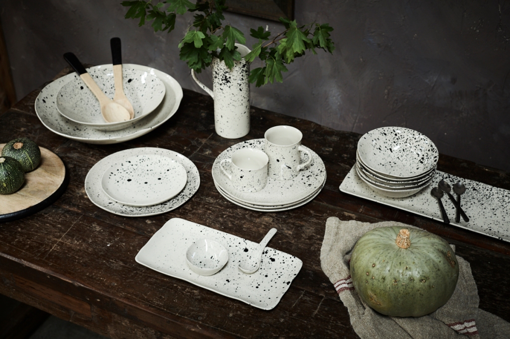 Black and white paint speckled ceramics on a dark wooden table with seasonal squashes